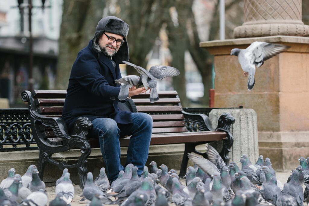 a-gray-haired-man-feeds-pigeons-while-sitting-on-a-min